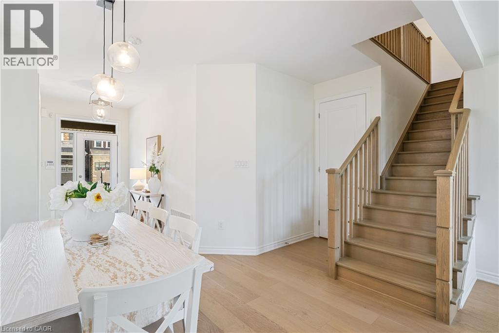 Hardwood flooring, natural wood staircase with balusters, contemporary pendant lighting, and a white paneled door - 68 Barkerville Drive, Whitby, ON