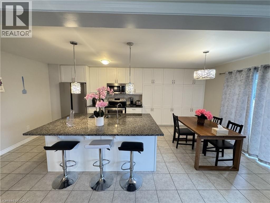 Kitchen featuring an expansive island with a stone countertop, white cabinetry, stainless steel appliances, and tile flooring - 67 Pointer Street, Cambridge, ON