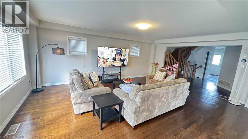 Wood-finish flooring throughout, multiple windows with blinds, and an open entryway to a wooden staircase with balusters - 67 Pointer Street, Cambridge, ON