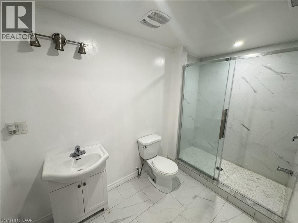 Glass-enclosed shower with white hexagon mosaic tile floor, white patterned wall tile, and a single vanity with a white ceramic sink - 67 Pointer Street, Cambridge, ON