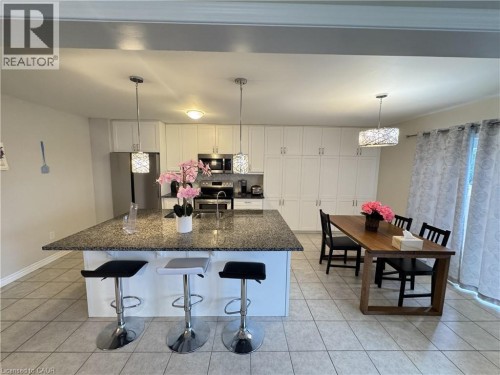 Kitchen featuring an expansive island with a stone countertop, white cabinetry, stainless steel appliances, and tile flooring - 67 Pointer Street, Cambridge, ON 