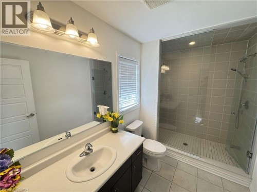 Vanity with integrated sink, expansive mirrored wall, brushed nickel three-light fixture, glass-enclosed shower with tile surround, and window with blinds - 67 Pointer Street, Cambridge, ON 