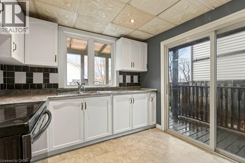 Kitchen featuring white cabinetry, patterned backsplash, light-colored flooring, and a sliding glass door to an outdoor area - 23 Frederick Avenue, Hamilton, ON