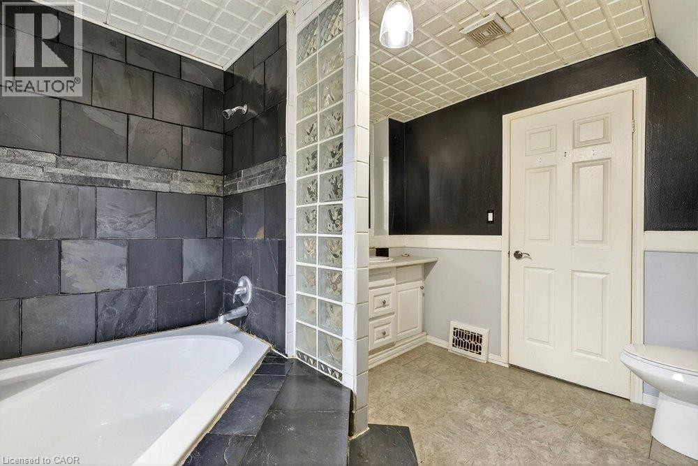Full-size bathtub with dark tile surround and glass block partition - 23 Frederick Avenue, Hamilton, ON