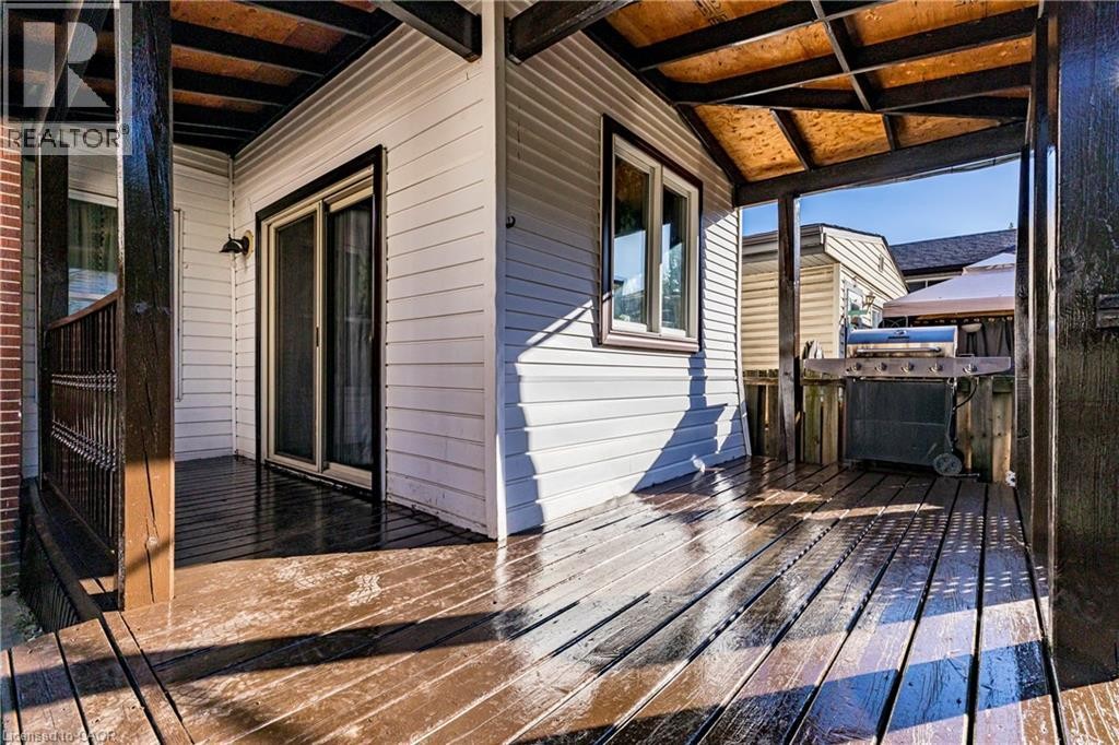 Covered outdoor deck with wood-finish flooring, white siding, and a sliding glass door - 23 Frederick Avenue, Hamilton, ON