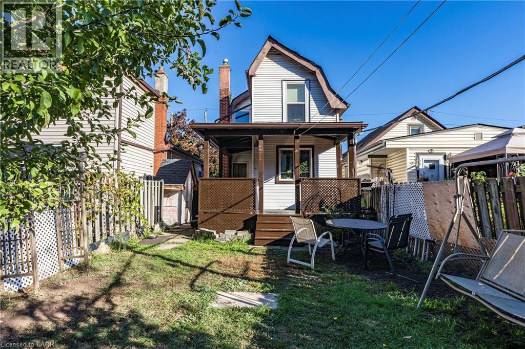 Rear exterior featuring white siding, a covered porch with lattice detailing, and an attached shed structure - 23 Frederick Avenue, Hamilton, ON
