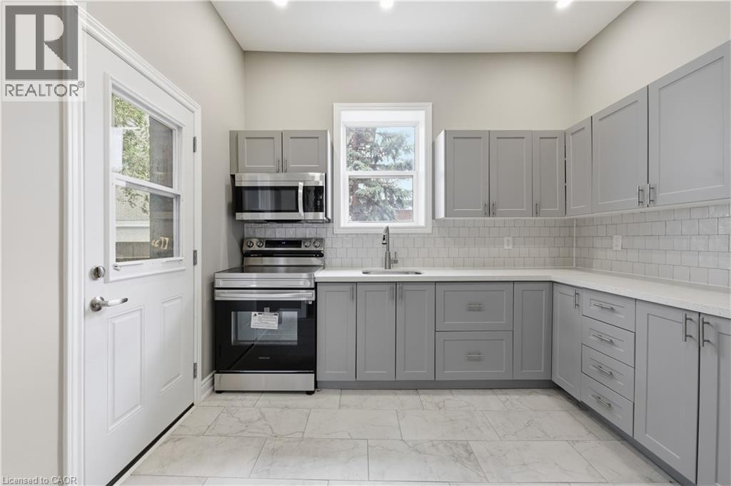Kitchen featuring grey shaker-style cabinetry, white subway tile backsplash, white countertops, and stainless steel appliances - 98 Duke Street Unit# 2Nd, Hamilton, ON