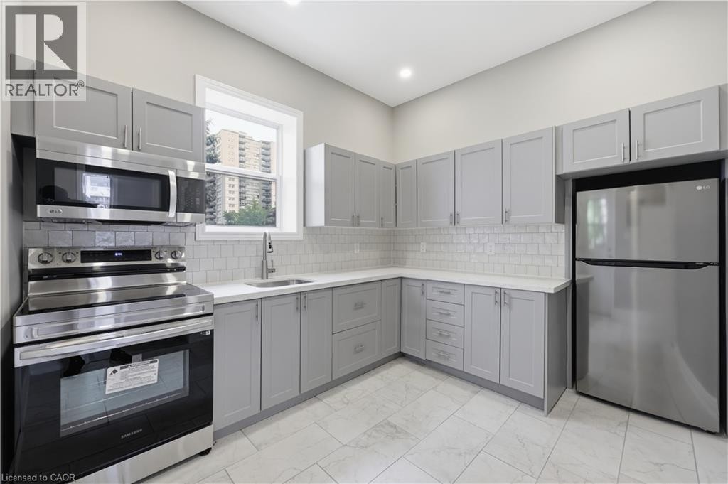 Light gray shaker-style cabinetry, stainless steel appliances, white subway tile backsplash, light-toned countertops, and light-colored floor tiling - 98 Duke Street Unit# 2Nd, Hamilton, ON