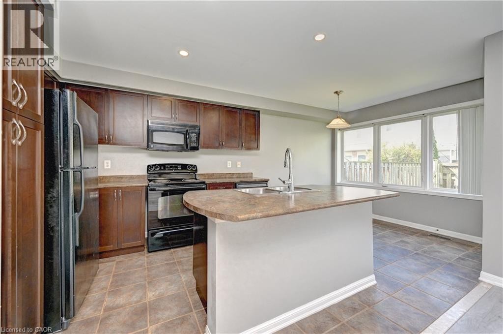 Kitchen featuring dark wood cabinetry, a center island with sink and integrated breakfast bar, black appliances, and tiled flooring - 103 Blackbird Circle, Cambridge, ON