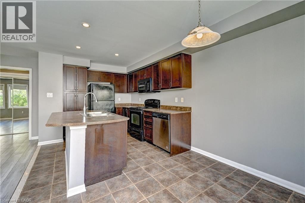 Kitchen featuring dark wood-finish cabinetry, a built-in pantry, stainless steel appliances, an island with an integrated sink, and tile flooring - 103 Blackbird Circle, Cambridge, ON