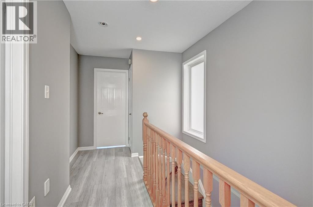 Hallway featuring light gray walls, recessed ceiling lighting, wood-finish flooring, and natural wood stair railing - 103 Blackbird Circle, Cambridge, ON