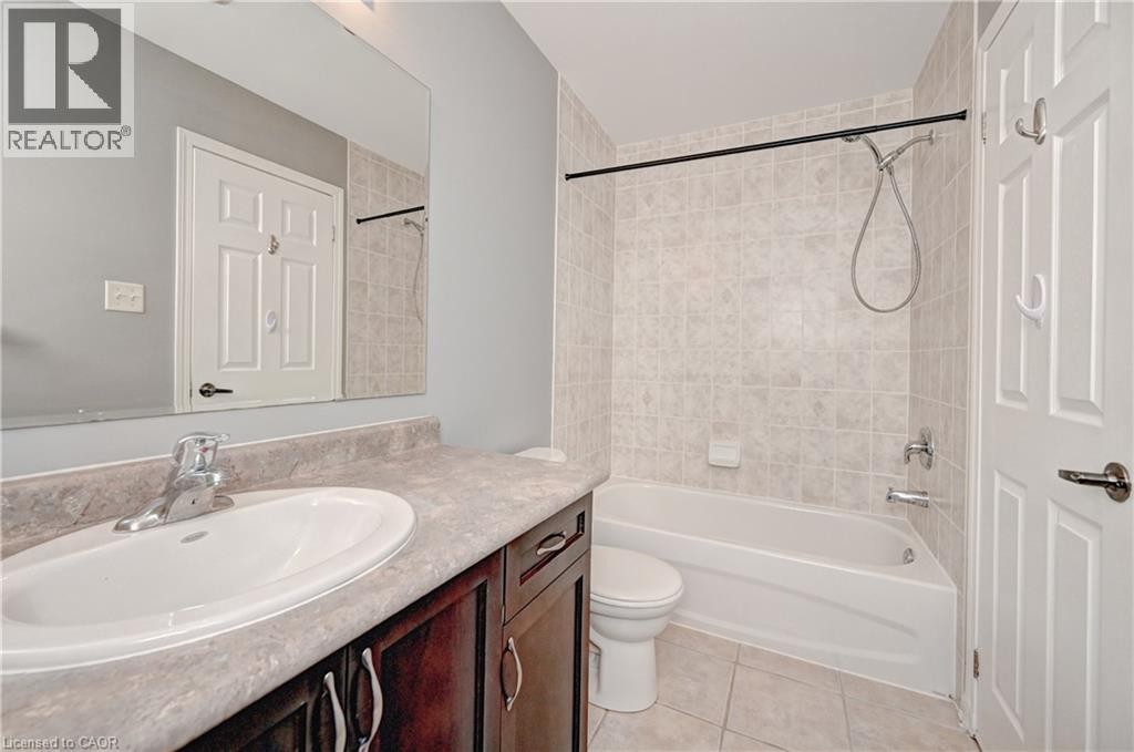 Built-in vanity with a single basin sink, laminate countertop, dark wood-finish cabinetry, tiled shower surround, and tiled flooring - 103 Blackbird Circle, Cambridge, ON
