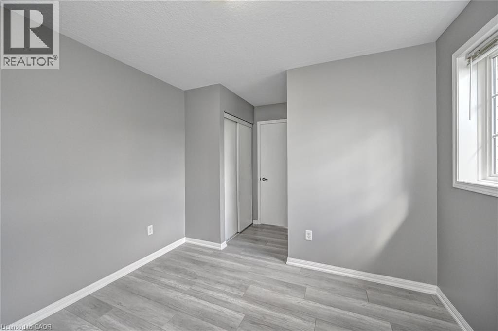Light gray wood-finish flooring, neutral gray painted walls, white trim, and a white framed window with blinds - 103 Blackbird Circle, Cambridge, ON