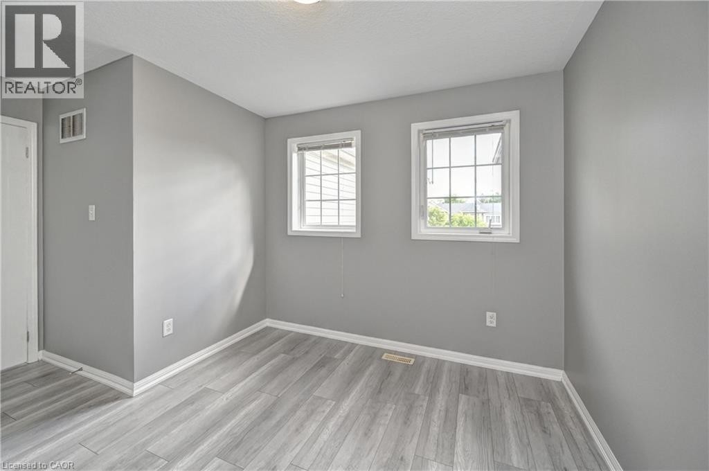 Wood-finish flooring with crisp white trim, two windows with grid detailing, and a flush mount ceiling light - 103 Blackbird Circle, Cambridge, ON