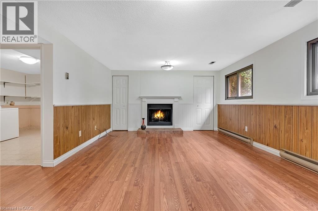 Spacious room featuring wood-finish flooring, a white mantel fireplace, and wood panel wainscoting - 7 Underhill Crescent, Kitchener, ON