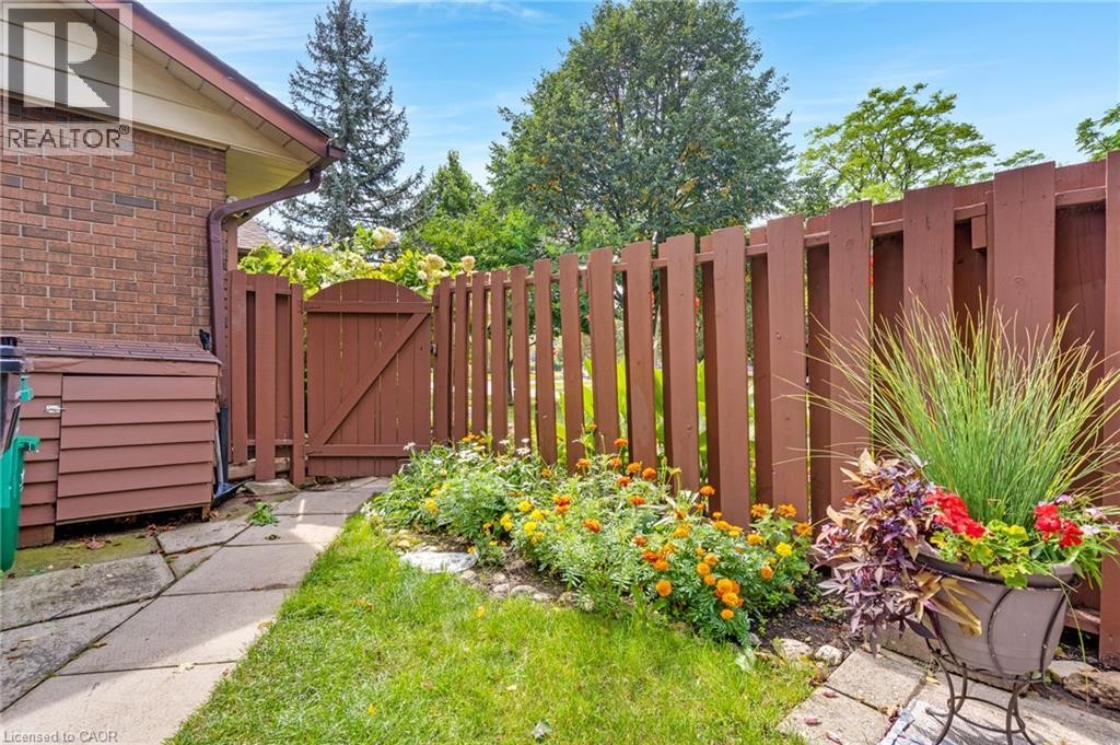Brick exterior with a brown wooden fence and gate, stone-paver walkway, and planted garden bed - 7 Underhill Crescent, Kitchener, ON