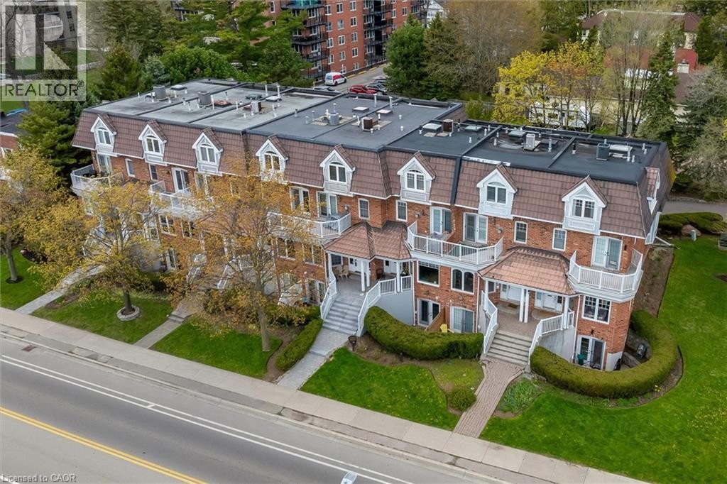 Brick facade property featuring multiple balconies with white railings, dormer windows, a brown mansard-style roof, and landscaped grounds - 1389 Lakeshore Road, Burlington, ON