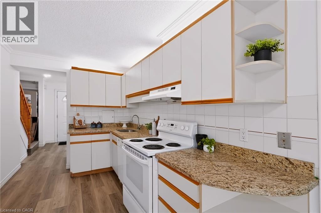 Kitchen featuring white cabinetry with wood trim, L-shaped countertops, white tiled backsplash, and wood-finish flooring - 121 University Avenue E Unit# 102, Waterloo, ON