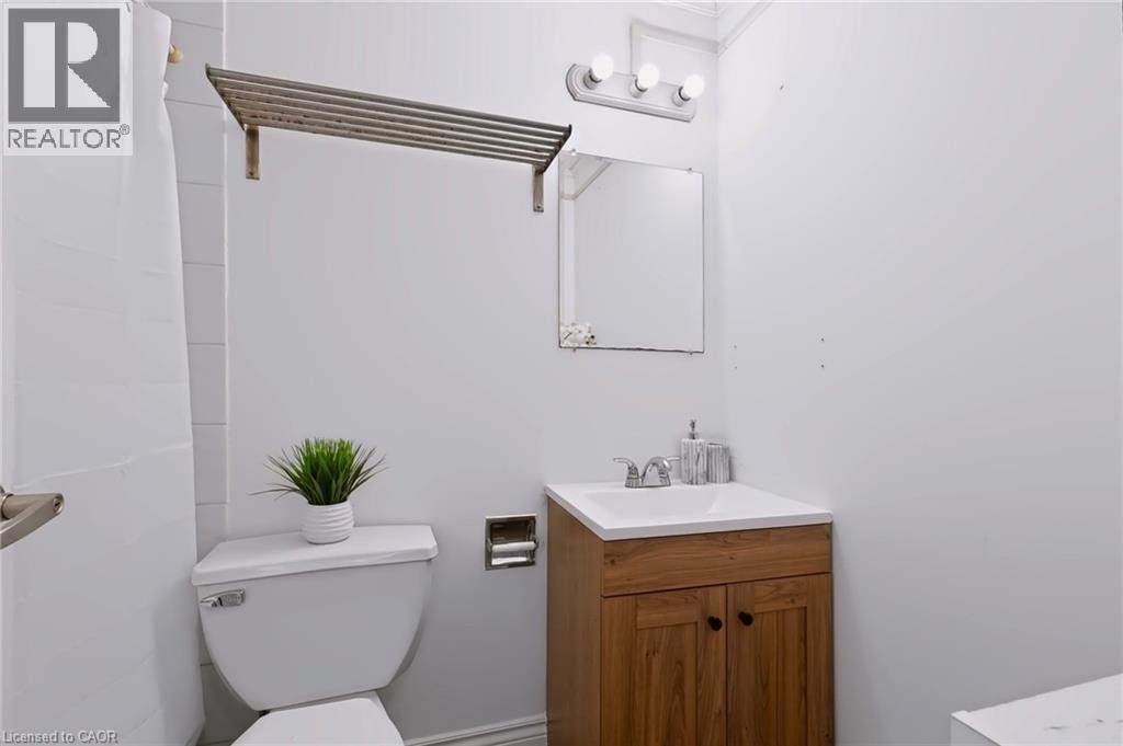 Wood-finish vanity with a white countertop and integrated sink, chrome faucet, and a wall-mounted mirror - 121 University Avenue E Unit# 102, Waterloo, ON