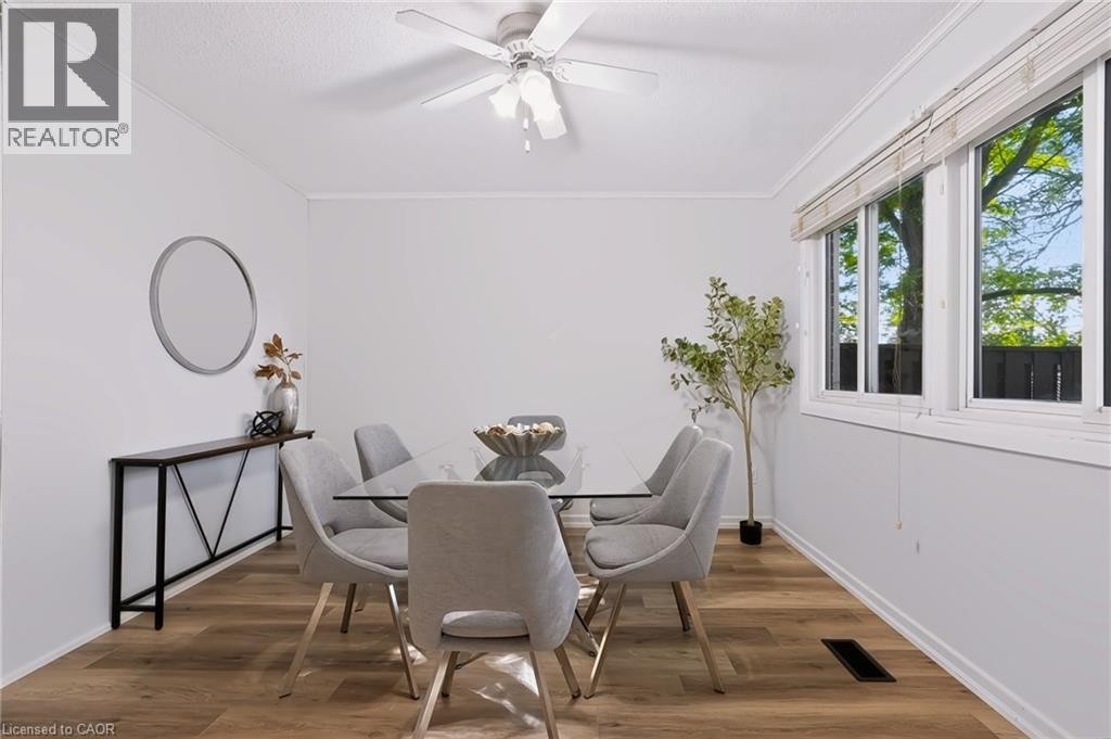 Bright dining space showcasing warm wood-finish flooring, a ceiling fan with integrated lighting, and expansive multi-panel windows flooding the room with natural light - 121 University Avenue E Unit# 102, Waterloo, ON