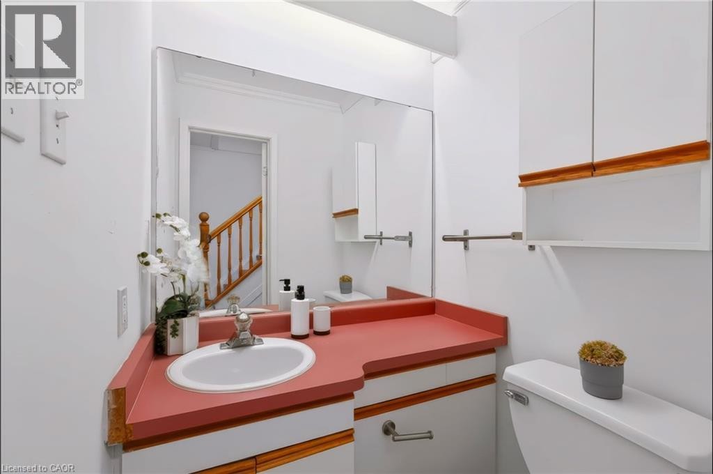 Modern bathroom featuring a distinctive coral-red countertop with integrated circular sink basin, wood-finish trim detailing, and large framed mirror with ample natural lighting from skylight above - 121 University Avenue E Unit# 102, Waterloo, ON