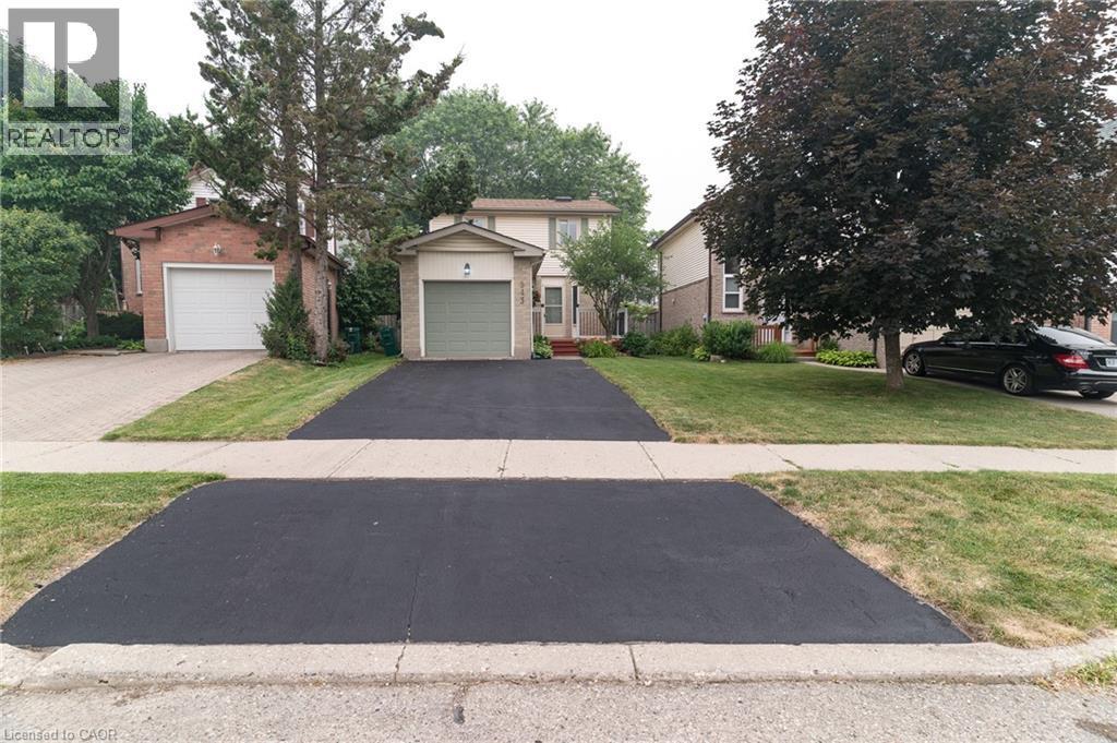Front-facing two-story residence featuring a single-car attached garage with a light green door, a paved driveway, and a front lawn with mature trees - 543 Drummerhill Crescent, Waterloo, ON