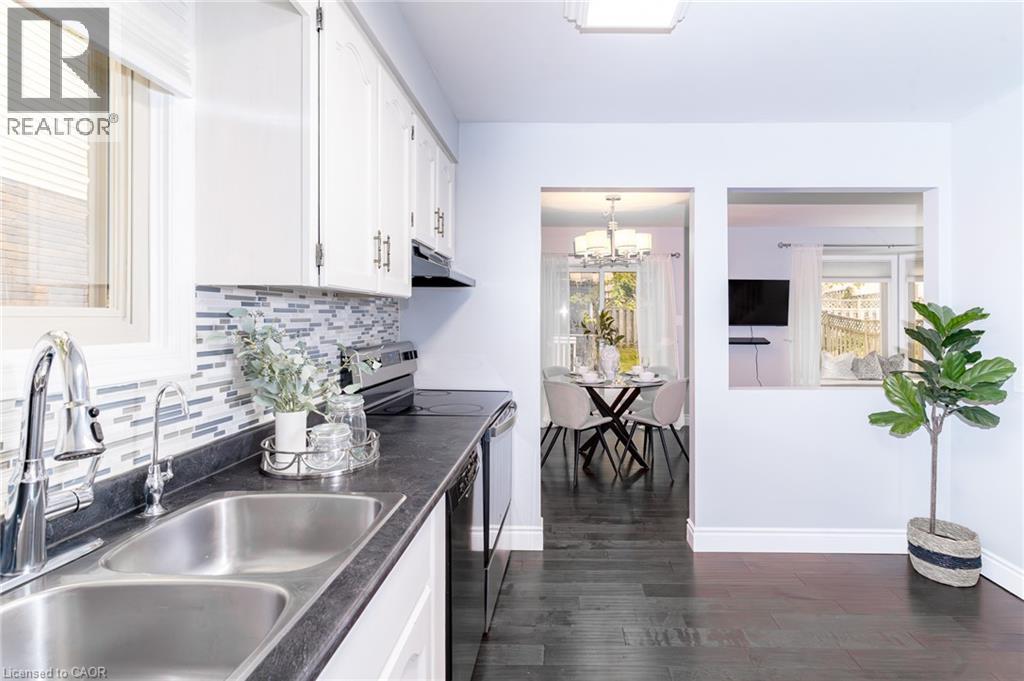 Kitchen featuring a double stainless steel sink, mosaic tile backsplash, white cabinetry, and dark countertops - 543 Drummerhill Crescent, Waterloo, ON