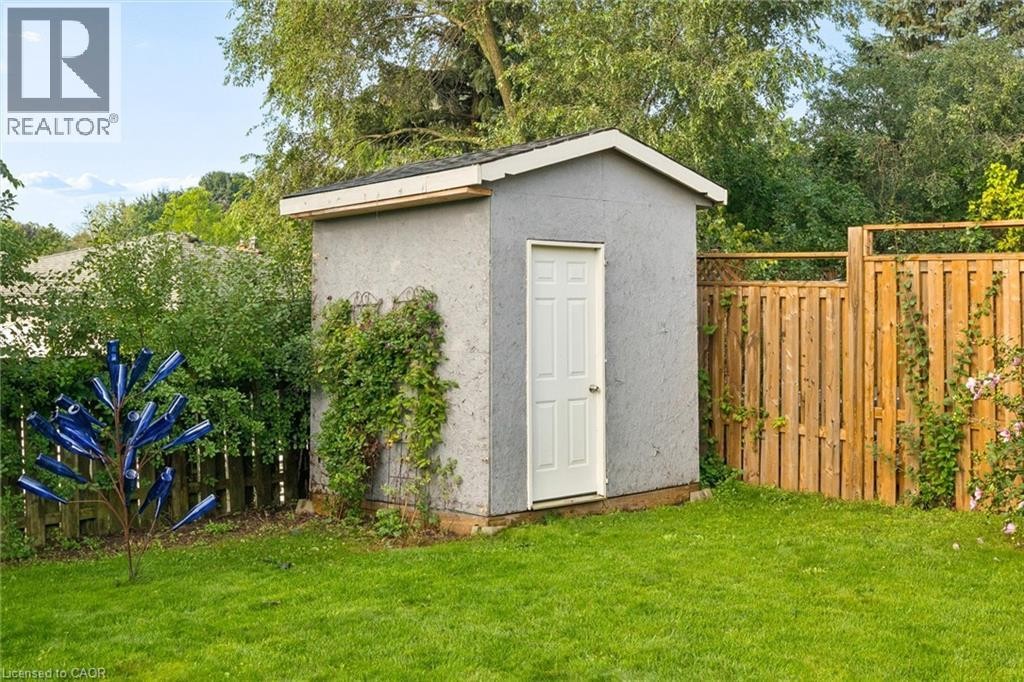 Grassed yard featuring a storage shed with a white door and a wood fence - 76 Cluthe Crescent, Kitchener, ON