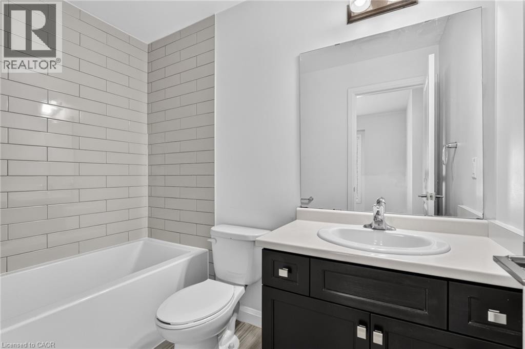 White subway tile surround, built-in bathtub, white toilet, dark wood-finish vanity with a white countertop, and an oval undermount sink - 1169 E Garner Road E Unit# 66, Ancaster, ON