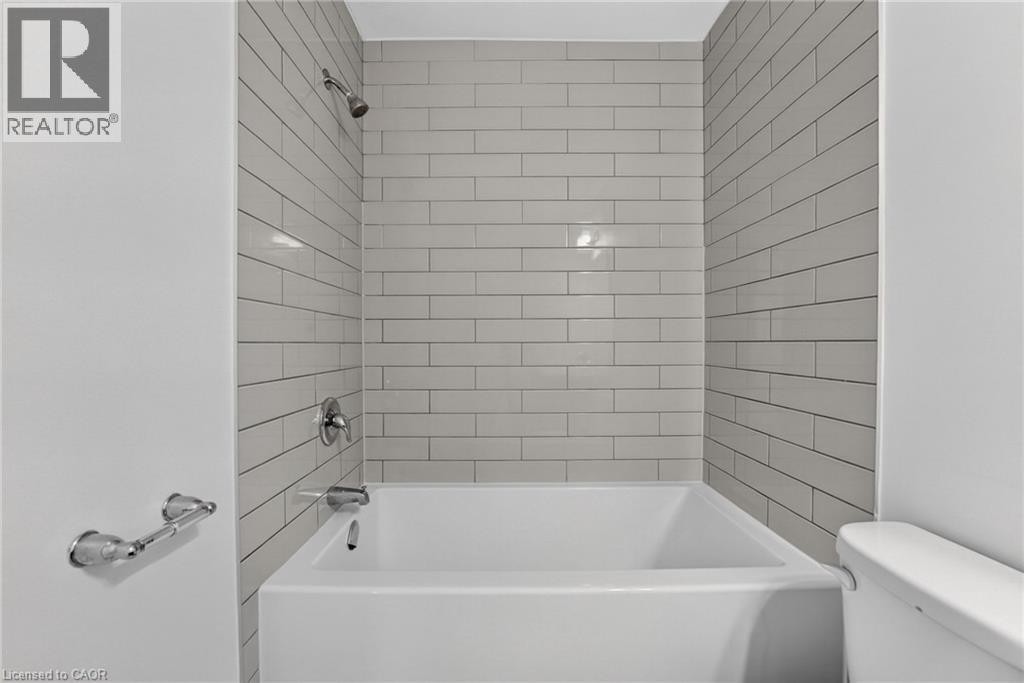 White bathtub with subway tile surround, chrome fixtures, and adjacent commode - 1169 E Garner Road E Unit# 66, Ancaster, ON