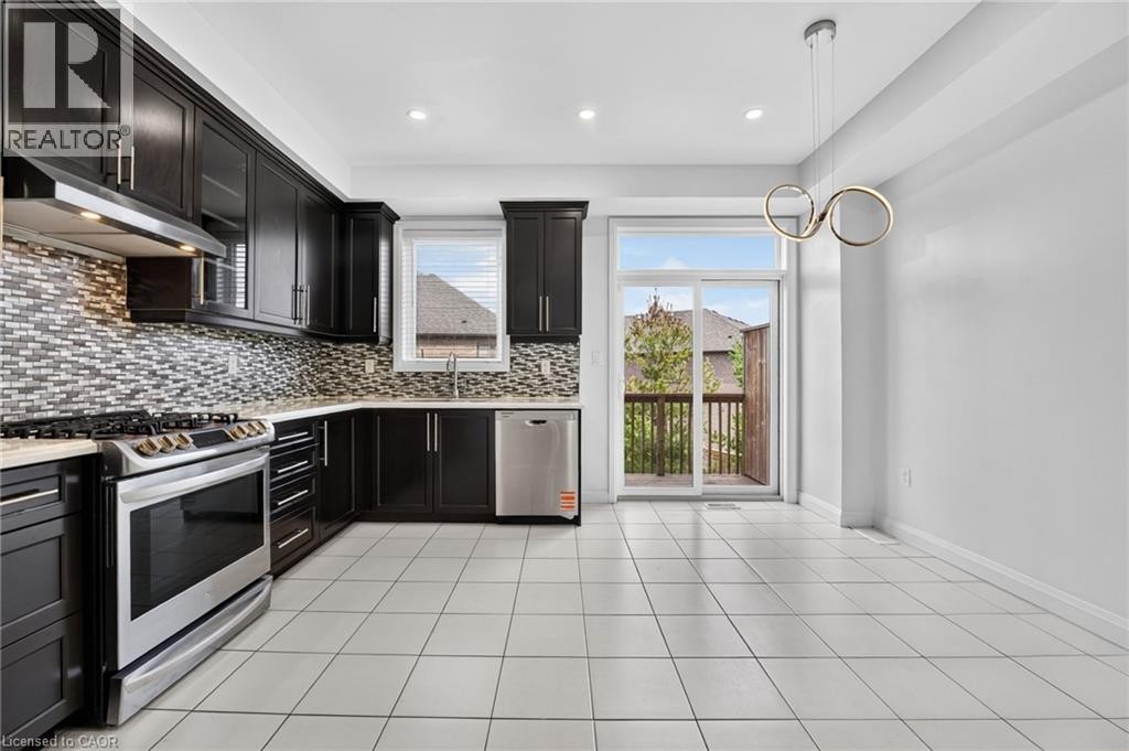 Kitchen featuring dark wood-finish cabinetry, stainless steel appliances, mosaic tile backsplash, and light-toned tile flooring - 1169 E Garner Road E Unit# 66, Ancaster, ON
