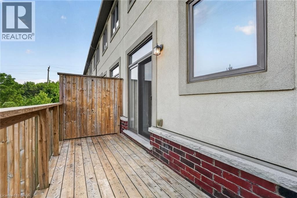 Wood-plank outdoor deck with wood privacy screen, exterior wall sconce, and red brick facade accent - 1169 E Garner Road E Unit# 66, Ancaster, ON