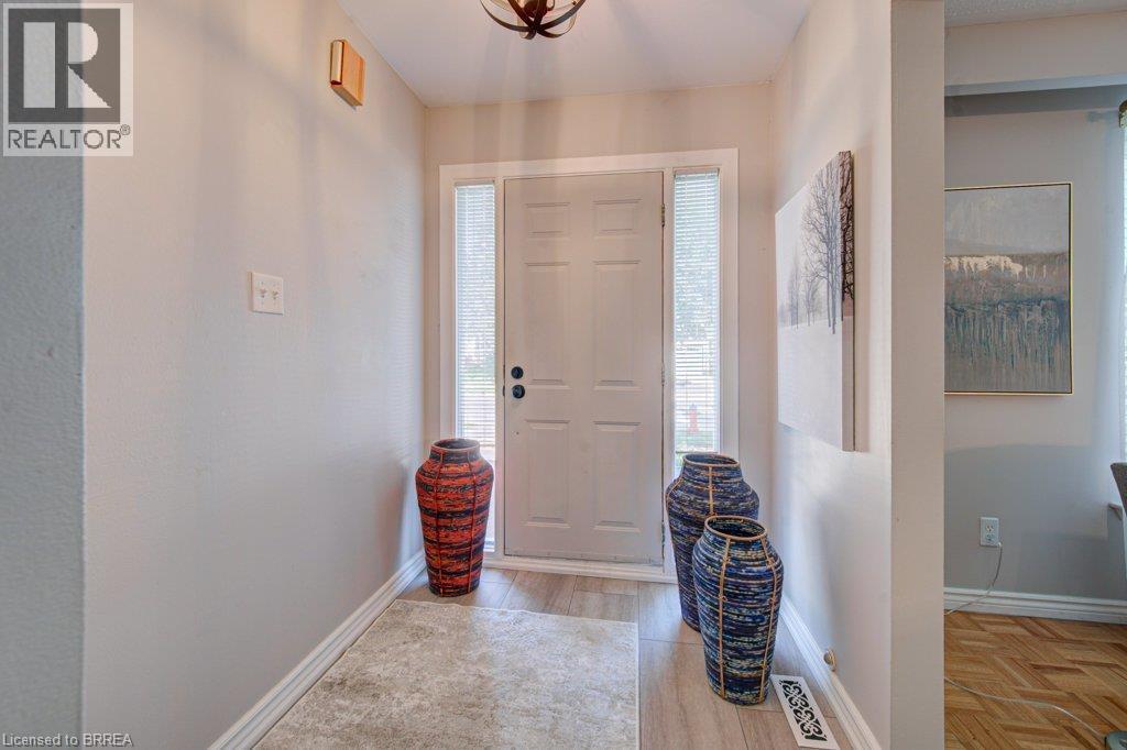 Entryway featuring a paneled door with side lights, wood-finish flooring, and a ceiling-mounted light fixture - 3158 Palmer Drive, Burlington, ON