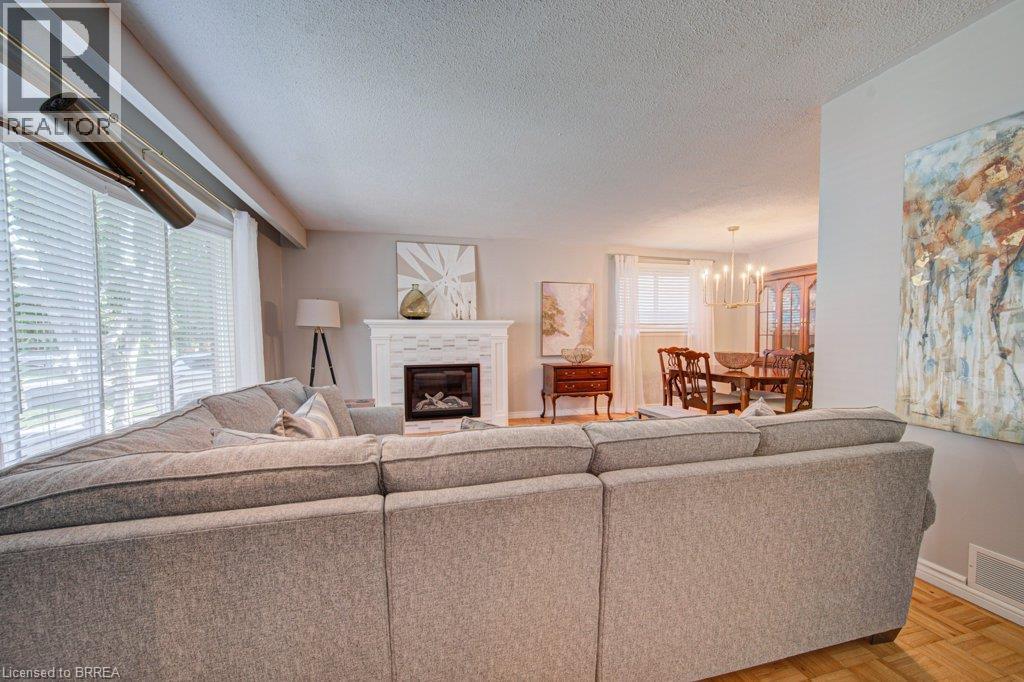 Living area featuring a fireplace with a tiled surround, wood-finish flooring, and window blinds - 3158 Palmer Drive, Burlington, ON