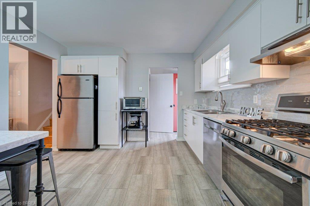 Kitchen featuring wood-finish flooring, white cabinetry, stainless steel appliances, and a tiled backsplash - 3158 Palmer Drive, Burlington, ON
