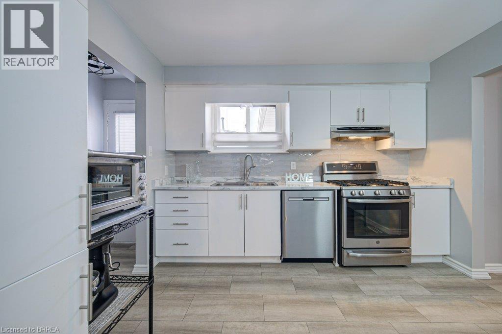 Modern kitchen featuring white cabinetry, stainless steel appliances, wood-finish flooring, a tiled backsplash, and a window - 3158 Palmer Drive, Burlington, ON