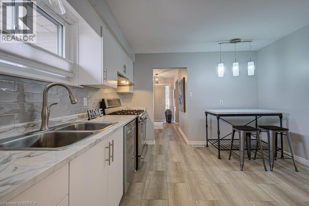 Kitchen featuring wood-finish flooring, white cabinetry, a double basin stainless steel sink, and a tiled backsplash - 3158 Palmer Drive, Burlington, ON