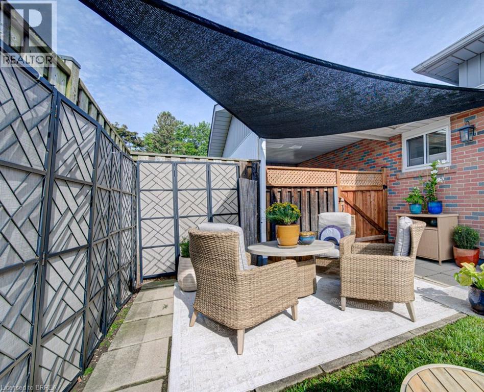 Patio space featuring a black shade sail, brick exterior, lattice-top wooden fencing, and decorative privacy screens - 3158 Palmer Drive, Burlington, ON