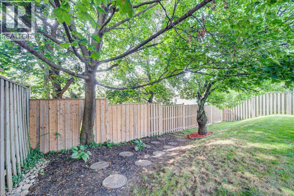 Expansive backyard featuring mature trees, a wooden privacy fence, a stepping stone path, and an inclined grassy area - 3158 Palmer Drive, Burlington, ON