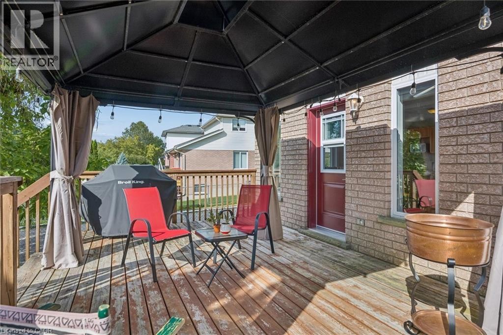 Spacious wooden deck featuring a built-in gazebo with curtains and string lighting, brick exterior, and a red entry door - 67 Apple Tree Drive, Kitchener, ON