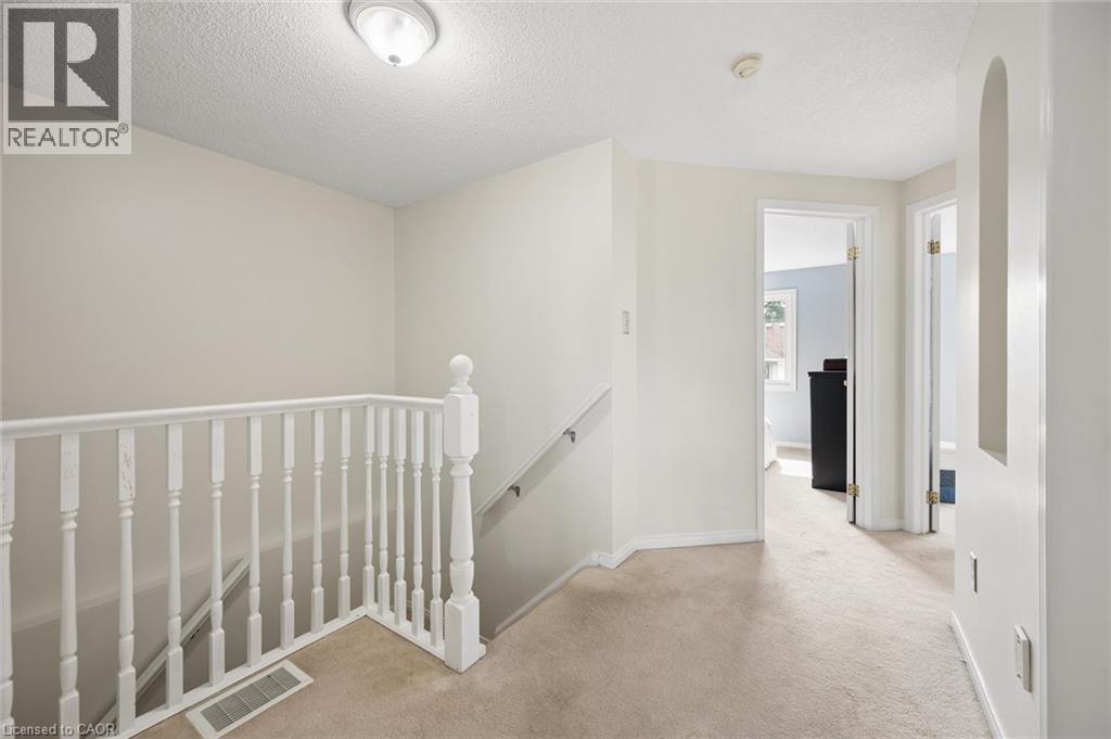 Carpeted hallway with white walls and a white spindle railing - 67 Apple Tree Drive, Kitchener, ON