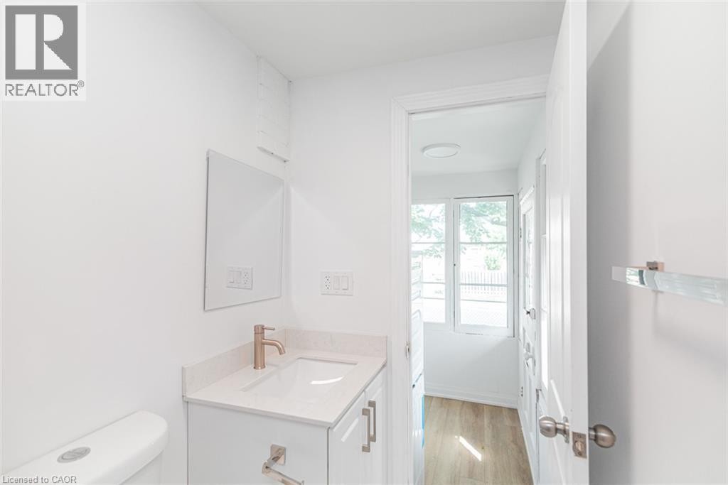 White vanity with a light-colored countertop and rose gold-tone faucet, accompanied by a rectangular mirror - 90 Belview Avenue, Hamilton, ON