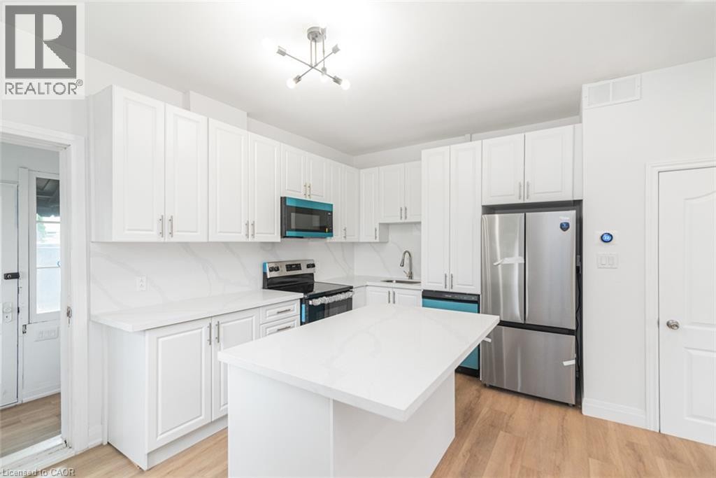 Kitchen featuring white cabinetry, a central island, stainless steel appliances, a white backsplash, and wood-finish flooring - 90 Belview Avenue, Hamilton, ON