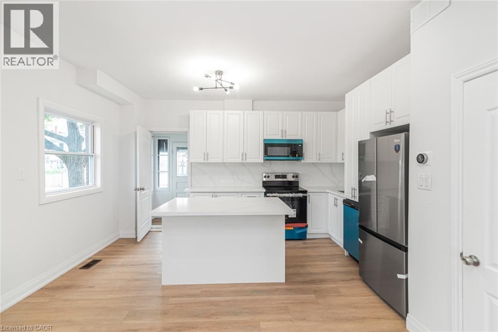 White shaker-style cabinetry, stainless steel appliances, light wood-finish flooring, a central island, and a contemporary chandelier - 90 Belview Avenue, Hamilton, ON