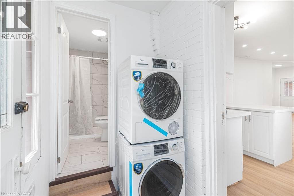 Dedicated laundry room featuring stacked front-load washers and dryers with modern controls, bright recessed lighting, and clean white cabinetry - 90 Belview Avenue, Hamilton, ON