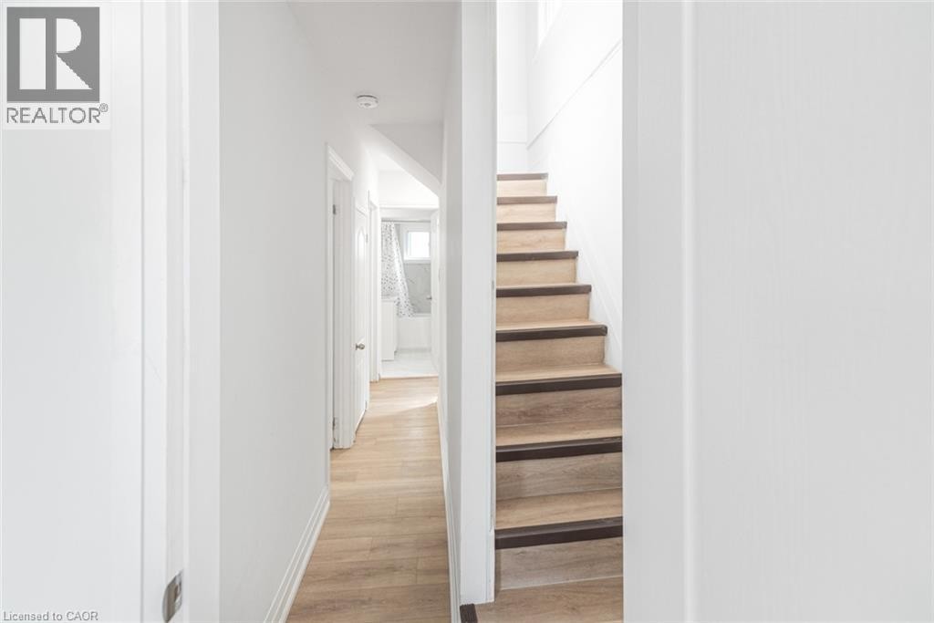 Wood-finish flooring throughout, white walls, and a staircase with wood-finish treads and dark risers - 90 Belview Avenue, Hamilton, ON