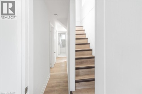 Wood-finish flooring throughout, white walls, and a staircase with wood-finish treads and dark risers - 90 Belview Avenue, Hamilton, ON 