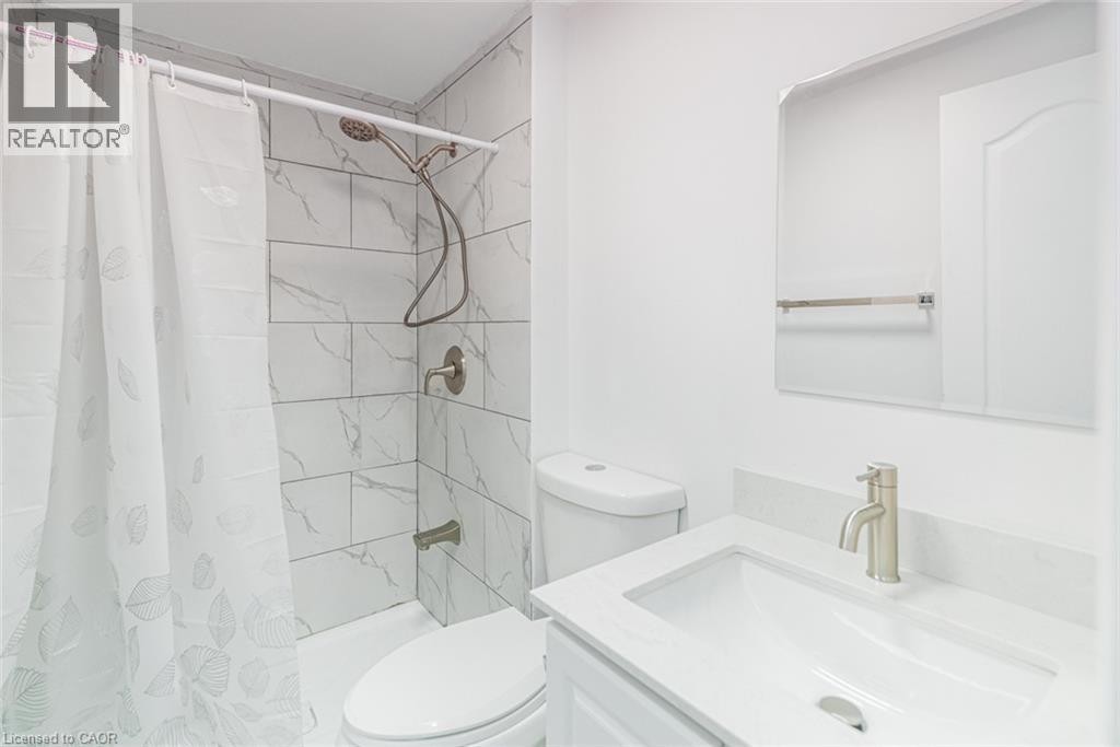 Bathroom featuring a white vanity with an integrated sink, brushed nickel faucet, large wall mirror, and subway tile shower surround - 90 Belview Avenue, Hamilton, ON