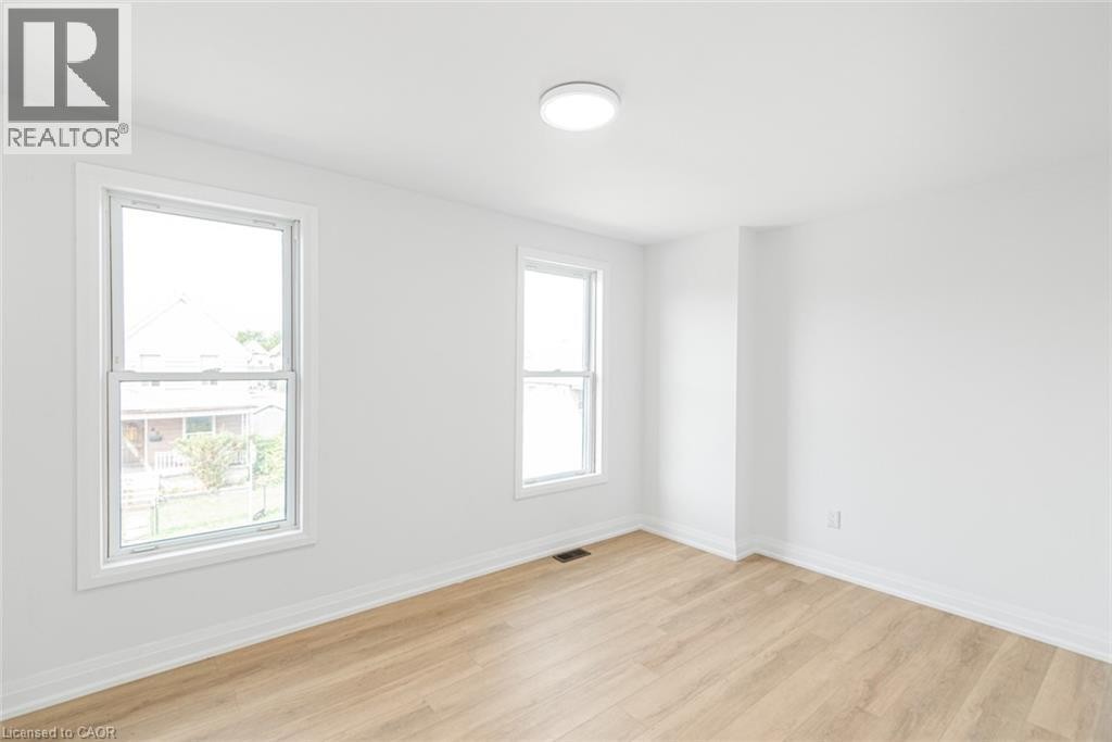 Bright room with two windows, a ceiling-mounted light fixture, light wood-finish flooring, and white trim - 90 Belview Avenue, Hamilton, ON