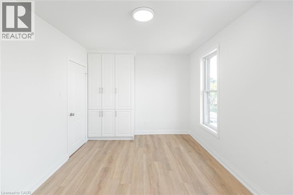 Wood-finish flooring, built-in white cabinetry, white interior door, and a single window - 90 Belview Avenue, Hamilton, ON